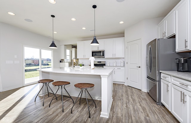 kitchen with appliances with stainless steel finishes, white cabinets, a sink, and light wood finished floors