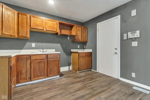 kitchen featuring brown cabinets, visible vents, light wood-style floors, a sink, and baseboards