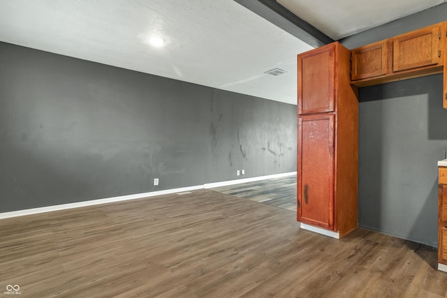 kitchen with brown cabinetry, wood finished floors, visible vents, and baseboards