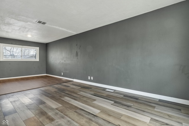 spare room featuring visible vents, baseboards, and wood finished floors