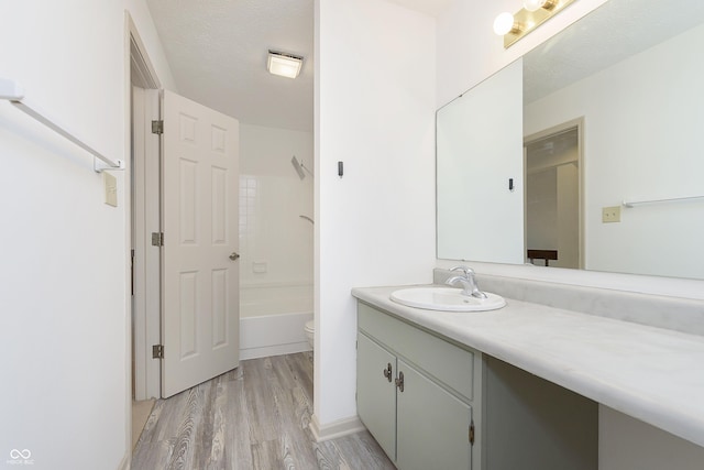 bathroom featuring bathing tub / shower combination, toilet, wood finished floors, a textured ceiling, and vanity