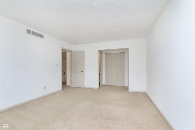 unfurnished bedroom featuring a closet, visible vents, light carpet, a textured ceiling, and baseboards