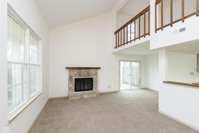 unfurnished living room with visible vents, baseboards, carpet, a stone fireplace, and high vaulted ceiling