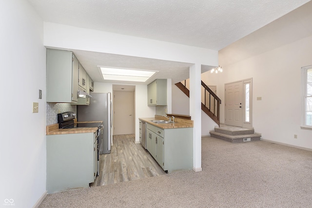 kitchen featuring a textured ceiling, light colored carpet, a sink, electric range oven, and tasteful backsplash