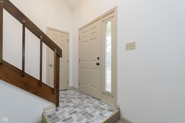 foyer with brick floor, stairway, and baseboards