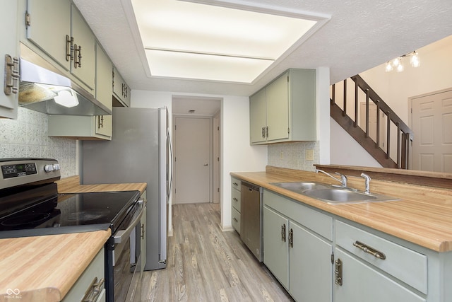 kitchen featuring light wood-style flooring, appliances with stainless steel finishes, a sink, under cabinet range hood, and green cabinetry