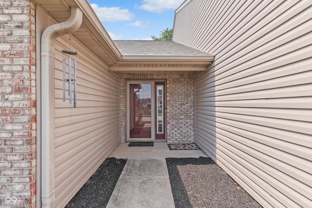 view of exterior entry with a shingled roof and brick siding