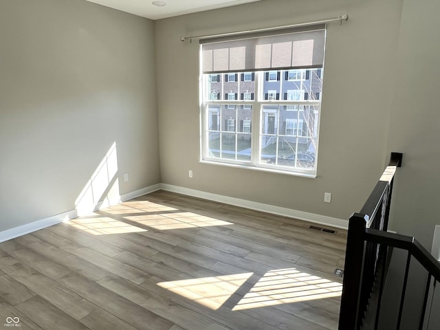 spare room featuring wood finished floors, visible vents, and baseboards