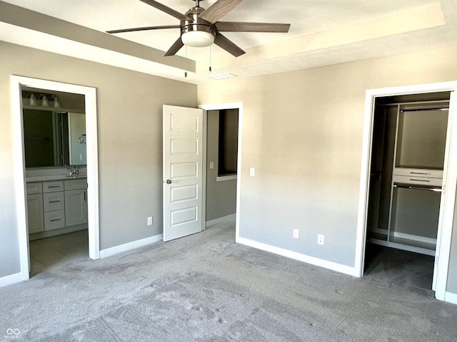 unfurnished bedroom with baseboards, a tray ceiling, light carpet, a closet, and ensuite bath