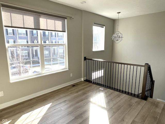 empty room featuring a notable chandelier, visible vents, baseboards, and wood finished floors