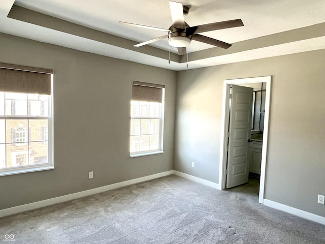 unfurnished bedroom featuring a ceiling fan, a tray ceiling, connected bathroom, carpet flooring, and baseboards