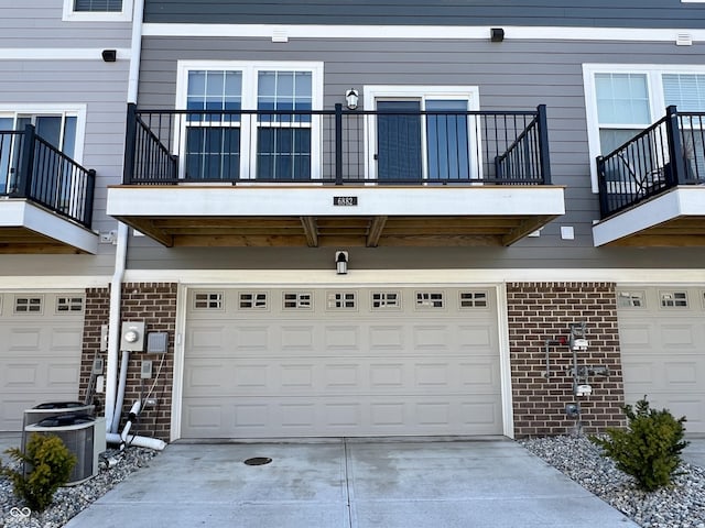 exterior space with a garage, cooling unit, brick siding, and concrete driveway