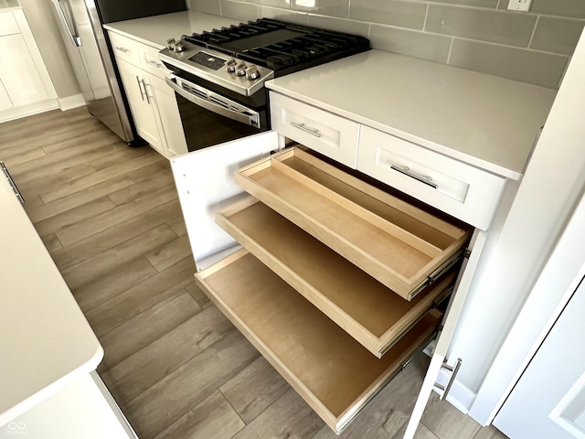 kitchen with light countertops, white cabinets, light wood finished floors, and stainless steel gas range oven