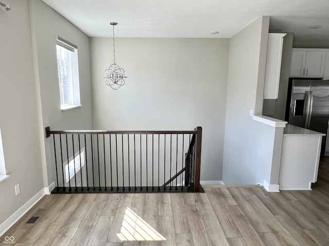 unfurnished dining area featuring an inviting chandelier, light wood-style floors, visible vents, and baseboards