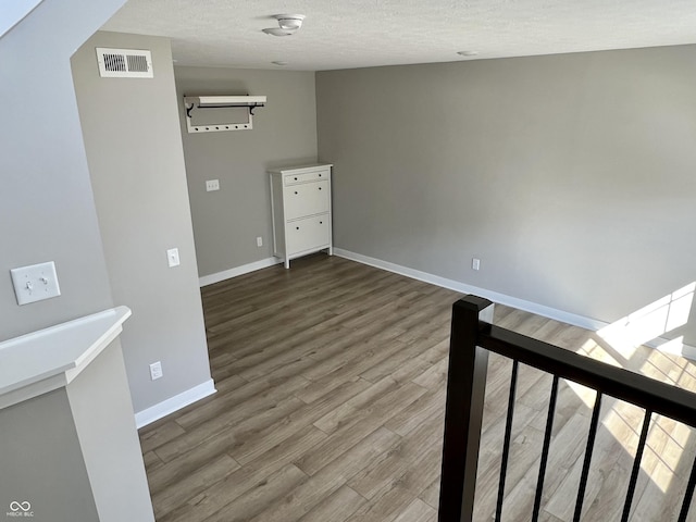 spare room with a textured ceiling, wood finished floors, visible vents, and baseboards