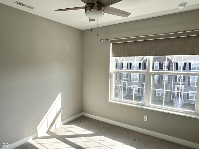 carpeted spare room with visible vents, baseboards, and a ceiling fan