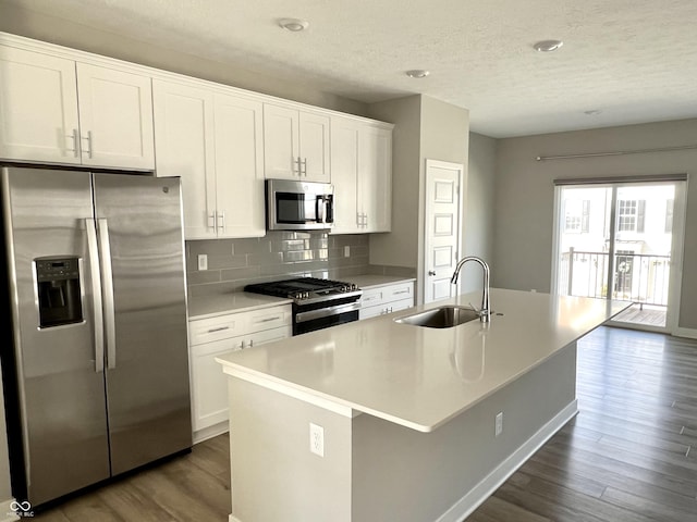 kitchen with dark wood-type flooring, an island with sink, appliances with stainless steel finishes, white cabinets, and a sink