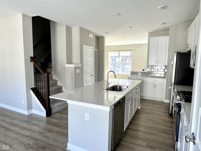 kitchen with a kitchen island with sink, a sink, tasteful backsplash, wood finished floors, and appliances with stainless steel finishes