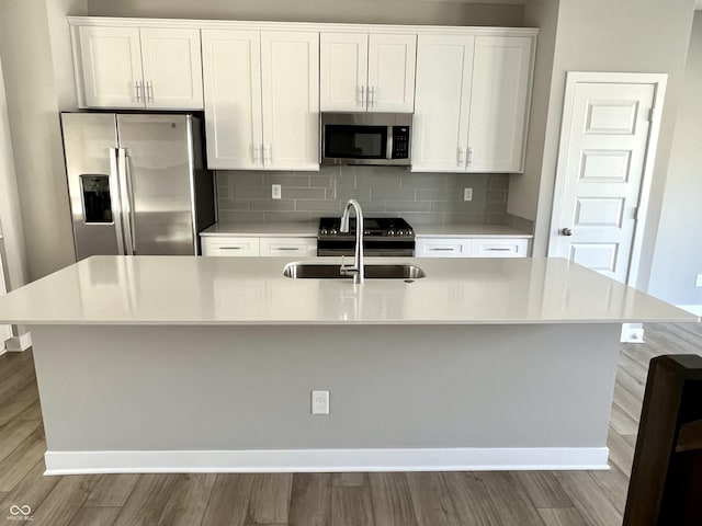 kitchen with a sink, backsplash, appliances with stainless steel finishes, white cabinetry, and a kitchen island with sink