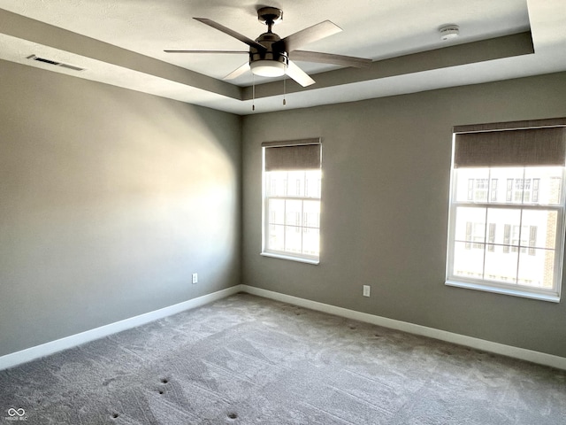 empty room featuring a raised ceiling, carpet, visible vents, and baseboards