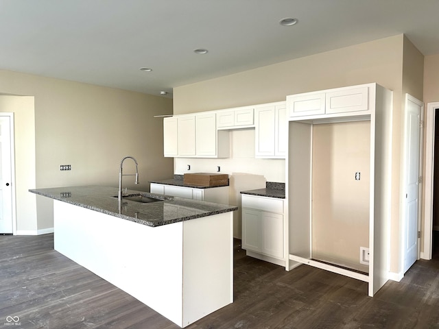 kitchen featuring a kitchen island with sink, a sink, dark stone countertops, dark wood finished floors, and white cabinetry