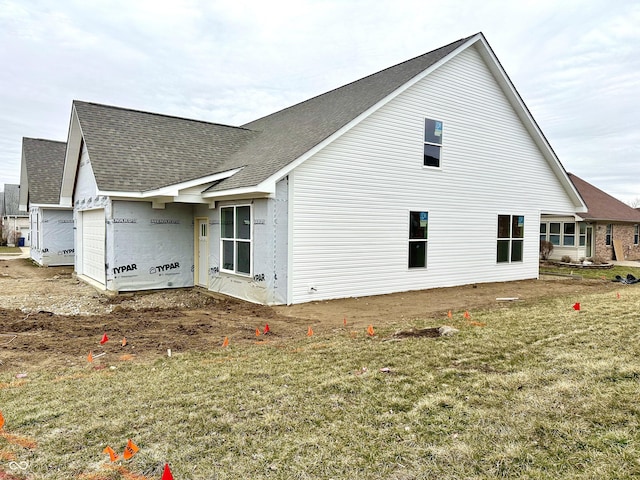 view of side of property with a garage, a lawn, and a shingled roof
