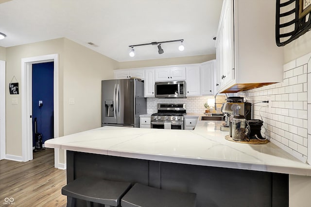 kitchen featuring stainless steel appliances, white cabinetry, a peninsula, and light stone countertops