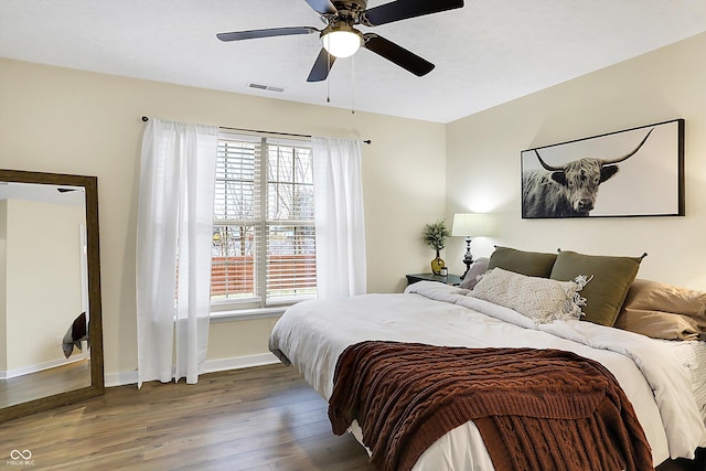 bedroom with a ceiling fan, visible vents, baseboards, and wood finished floors