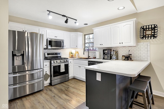 kitchen with a breakfast bar, stainless steel appliances, light wood-style floors, a sink, and a peninsula