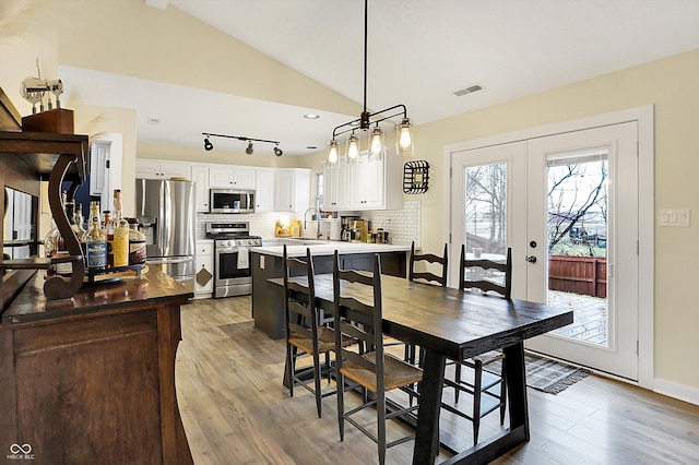 dining space with lofted ceiling, french doors, light wood finished floors, and visible vents