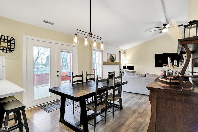 dining space featuring a large fireplace, visible vents, vaulted ceiling, and wood finished floors