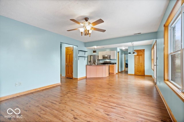 unfurnished living room featuring visible vents, light wood-style flooring, a ceiling fan, a textured ceiling, and baseboards