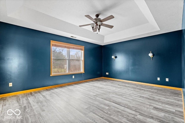 unfurnished room featuring a ceiling fan, a raised ceiling, baseboards, and wood finished floors