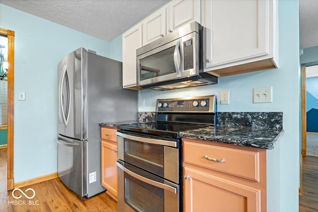 kitchen featuring dark stone countertops, light wood finished floors, appliances with stainless steel finishes, a textured ceiling, and white cabinetry