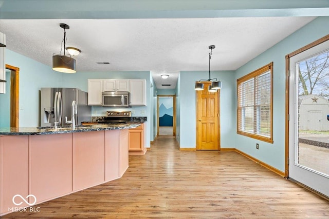 kitchen featuring pendant lighting, dark stone countertops, a textured ceiling, stainless steel appliances, and light wood finished floors