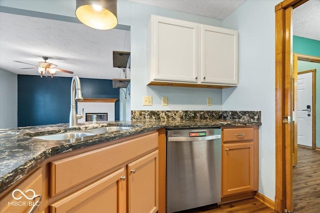 kitchen with wood finished floors, a sink, a textured ceiling, dishwasher, and a brick fireplace