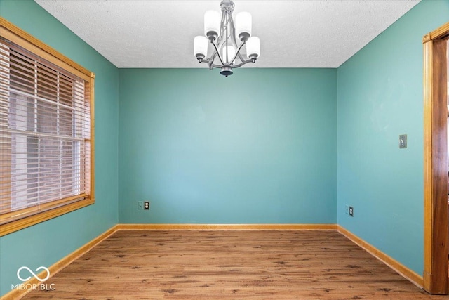 unfurnished room with a notable chandelier, wood finished floors, baseboards, and a textured ceiling