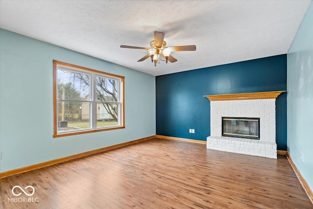 unfurnished living room featuring a ceiling fan, wood finished floors, baseboards, a textured ceiling, and a brick fireplace