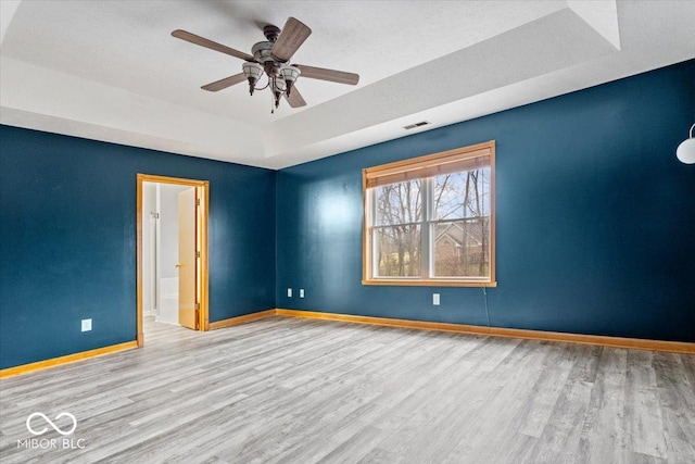 unfurnished room with visible vents, baseboards, a tray ceiling, wood finished floors, and a ceiling fan