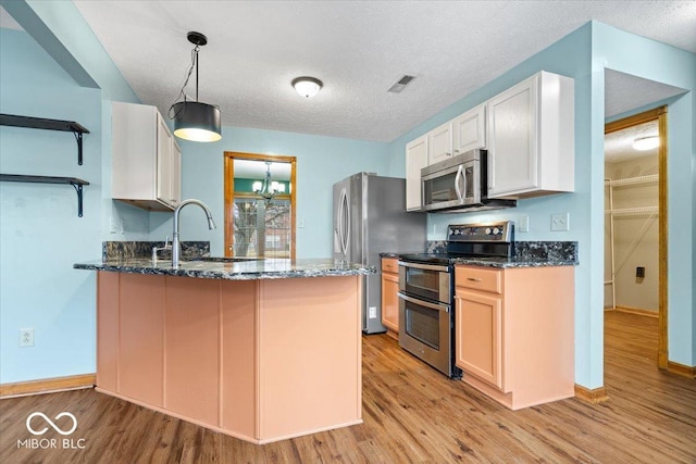 kitchen with dark stone countertops, a peninsula, light wood-style flooring, a sink, and stainless steel appliances