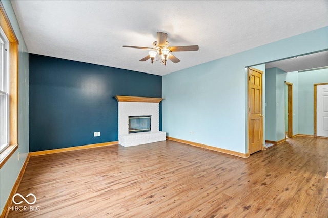 unfurnished living room with baseboards, wood finished floors, ceiling fan, and a fireplace