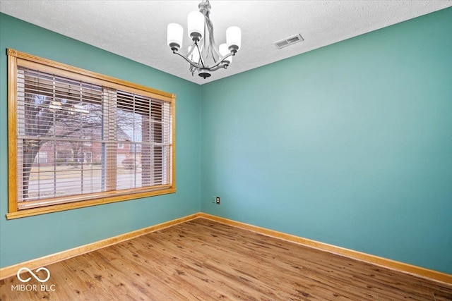 unfurnished room featuring visible vents, a textured ceiling, wood finished floors, an inviting chandelier, and baseboards