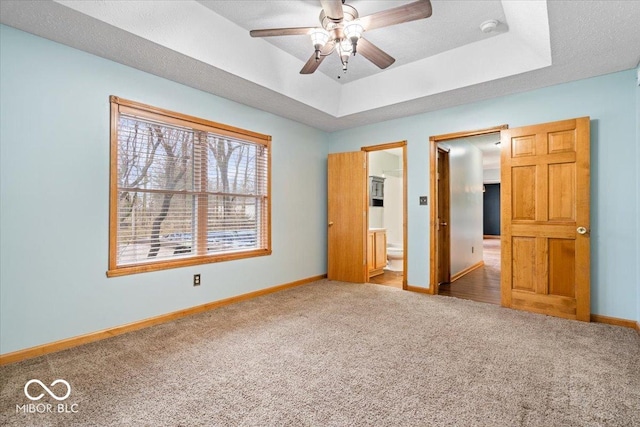 unfurnished bedroom featuring a tray ceiling, baseboards, ensuite bath, and carpet flooring