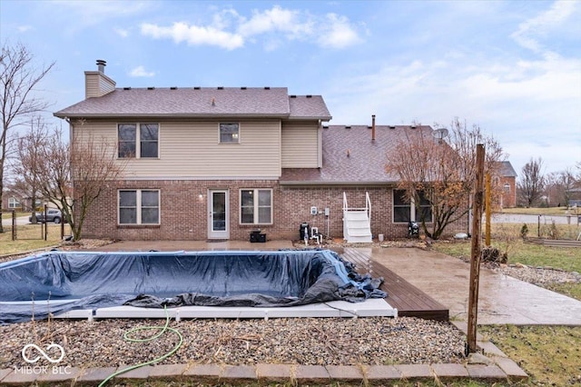 rear view of property featuring a fenced in pool, brick siding, and a chimney