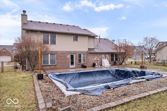 rear view of house featuring brick siding, a fenced in pool, fence, a lawn, and a chimney