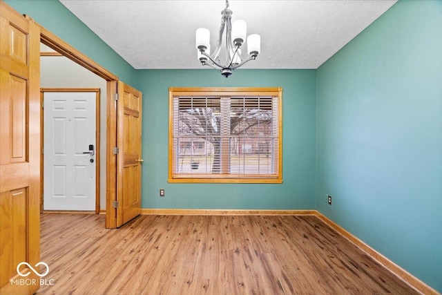 unfurnished dining area featuring a textured ceiling, baseboards, a notable chandelier, and light wood finished floors