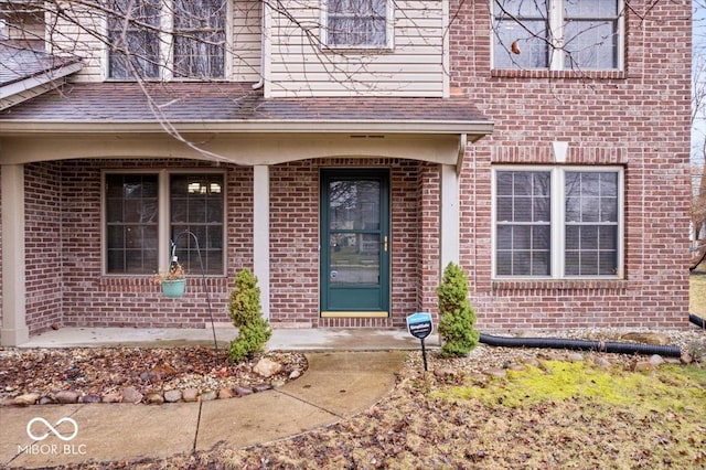 doorway to property with brick siding and a shingled roof