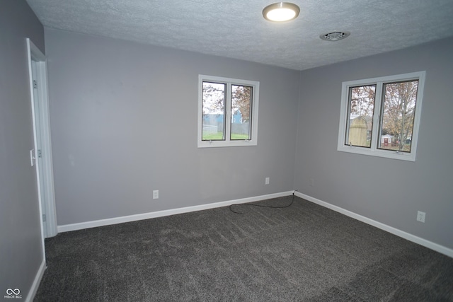 unfurnished room with dark colored carpet, visible vents, a textured ceiling, and baseboards