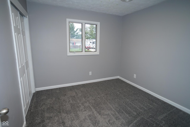 unfurnished bedroom featuring a textured ceiling, dark colored carpet, a closet, and baseboards