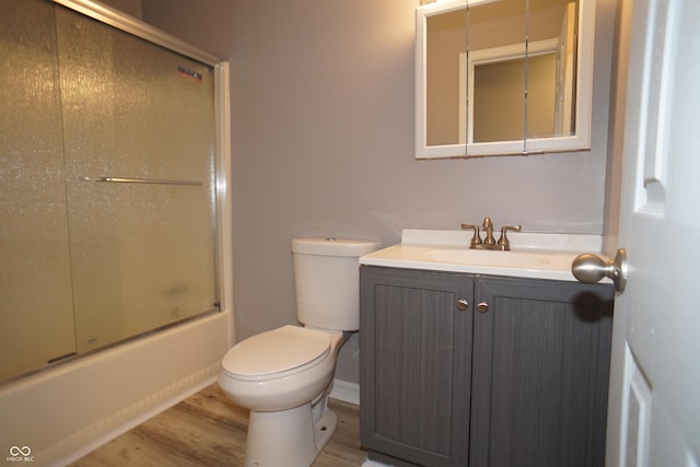 bathroom featuring vanity, combined bath / shower with glass door, wood finished floors, and toilet